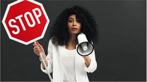 Concerned lady, long frizzy hair, wearing white top holding a stop sign and a megaphone trying to atract customers